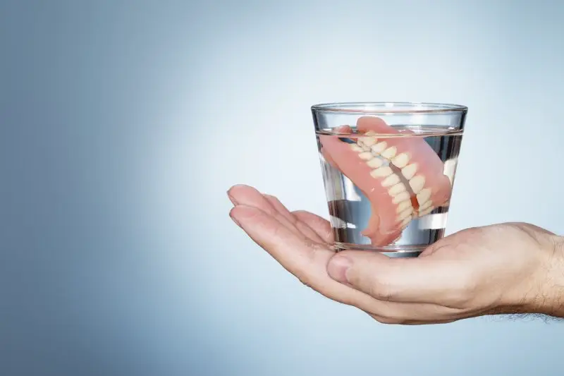 hand holding a glass of water with dentures